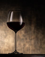 Elegant stemmed glass goblet filled with red wine placed on table against blurred shabby background