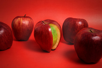 entre varias manzanas rojas una es verde por dentro, sobre fondo rojo © mateo