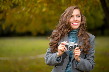 Beautiful woman wearing bright clothes take photos in autumn park over yellow tree background