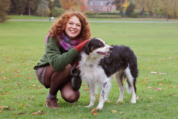 Naklejka na ściany i meble jeune et jolie femme rousse dans un parc arboré en automne avec des feuilles mortes promenant un grand chien en laisse 