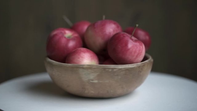 Red apples in wooden bowl rotate on white table. Loopable moving image.