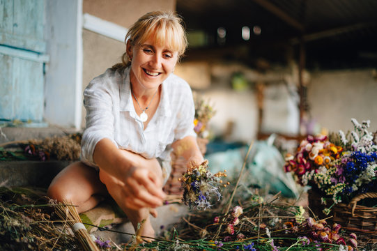 Happy woman farmer makes beautiful bouquets with a bunch of dried flowers grown in the country. Positive female florist makes bouquets for sale.