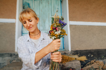 Portrait of a beautiful rural woman with a bouquet of dried flowers on a wall background. Focus on...