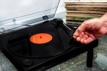 hand placing a vinyl record on a record player with a stack of vinyls behind