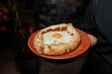 The waiter's hands in black gloves hold two traditional khachapuri with cheese and an egg