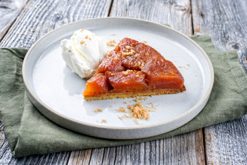 Traditional French tarte tatin with apples and ice cream offered as close-up on a modern Nordic design plate with rustic background
