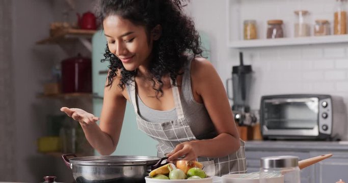 Beautiful woman preparing food at kitchen. She open boiler and smell soup with smile. Housewife preparing food at home.
