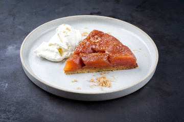 Traditional French tarte tatin with apples and ice cream offered as close-up on a modern Nordic design plate with rustic background