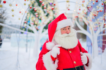Portrait of an elderly man dressed as santa claus on the background of a christmas tree outdoors.