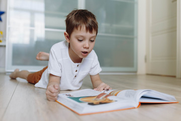 A boy is reading a book on the floor at home. Image with selective focus
