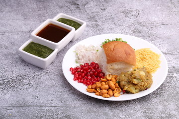 Dabeli is an Indian snack item served with Pomegranate Seeds and Cilantro in white ceramic plate. with green chutney and tamrind chutney.