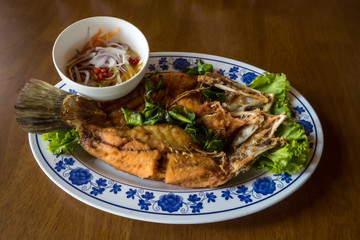 Fried sea bass fish in white plate with spicy and sweet sauce in Thai style .  crispy Thai style deep fried whole sea bass fish served with spicy mango sauce. crispy deep fried sea bass 