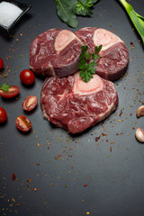 
three slices of ossobuco meat, on black background with cuanco with salt cherry tomatoes parsley and seasoning