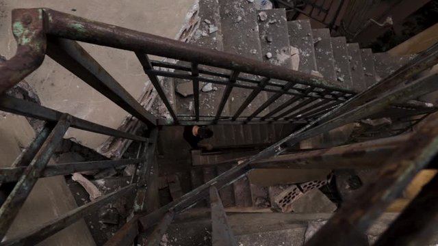 Beirut Lebanon explosion aftermath: looking downstairs at Caucasian person walking down interior stairs covered with debris, rubble, and fragments of building material scattered on staircase, static