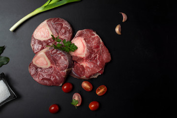 
three slices of ossobuco meat, on black background with cuanco with salt cherry tomatoes parsley and seasoning