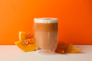 Glass of pumpkin latte, leaf and pumpkin on orange background