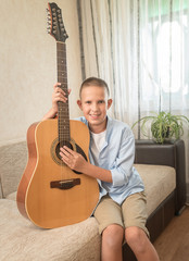 Cute happy child in a blue shirt with a guitar on the background of the window.