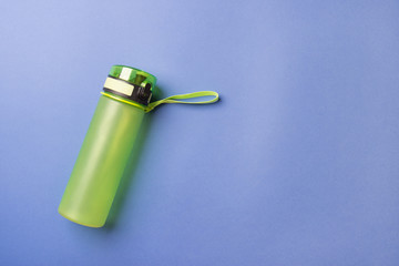 green plastic sport bottle lying on left side of blue background with copy space