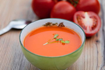A bowl with the traditional Spanish Gazpacho soup with some tomatoes on the background