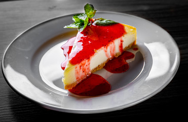 Strawberry cheesecake served on white plate on black wooden table background