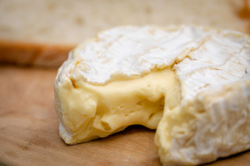 French Camembert cheese over a wooden table with some bread slices on the background