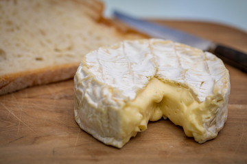 French Camembert cheese over a wooden table with some bread slices on the background