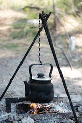 Smoked tourist kettle hanging on a tripod on campfire. Camping, local tourism. Vertical orientation.