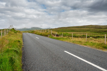 Fototapeta na wymiar Small asphalt road in Connemara, county Galway, Ireland, Nobody, Dramatic cloudy sky.