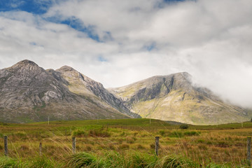 Beautiful mountains in Connemara, county Galway, Ireland; Warm sunny day, Clouds over peaks, Vast green fields.
