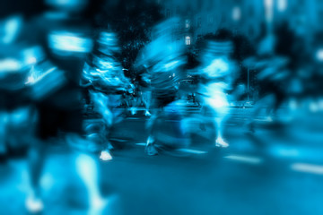 Motion blurred image of running athletes. Silhouettes of abstract unrecognizable people, night city, illumination bokeh. Active healthy lifestyle, sport