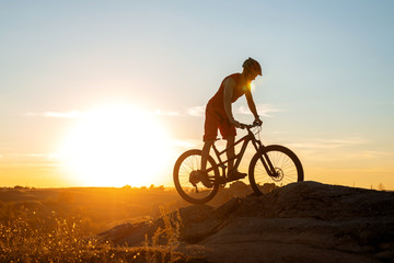A cyclist rides a mountain bike on the rocks during sunset, a copy of the free space.