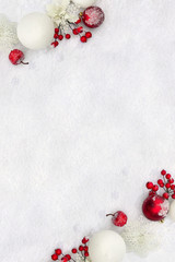 Christmas decoration. Frame of twigs christmas red berries, apple, red and white balls, white openwork flowers on snow with space for text. Top view, flat lay