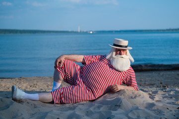 An elderly man in a striped retro swimsuit sunbathes on the beach. An old gray-haired bearded man...