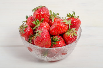 Ripe red strawberries in a bowl on a white wooden table