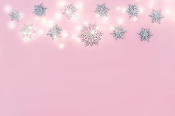 Christmas decor snowflakes with garland on pink background. Copy space.