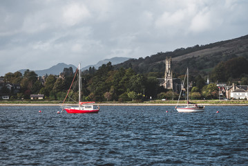 Small sailboats anchored on mooring near the shores of Firth of Clyde. Rhu, Scotland, UK. Old...