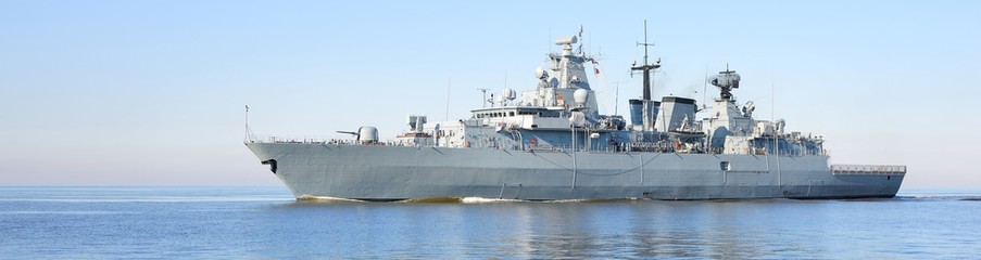 Large grey modern warship sailing in still water. Clear blue sky. Baltic sea, Germany. Global...