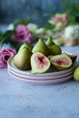 Ripe whole half and sliced figs among flavored green leaves of herbs and colorful flowers