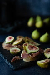 Bread with ham and fresh figs served on a black stone plate.