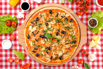 Rustic pizza with chicken meat, cheese, tomato, olive, mushrooms and tomatoes sauce, served on a wooden board for a dinner in italian restaurant background, top view. Classic Italy food. Close up