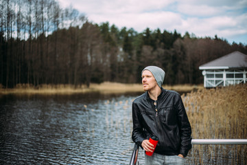 Pensive man in a leather jacket and hat stands and thinks outdoors.