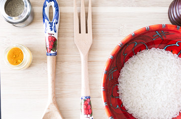 Plano cercano de un rojo tazón con granos de arroz blanco dentro junto a rústicos utensillos de...