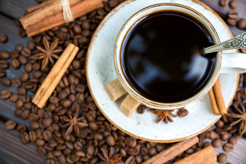 White cup of coffee with cinnamon and anise stars on a dark wooden background