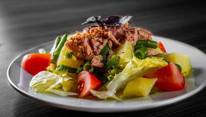 Salad nicoise. Tuna, with green beans, tomatoes, potatoes and a vinaigrette mustard dressing in white plate on black wooden table background
