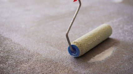 A worker applies the primer to the concrete floor with a roller. Applying a primer to the floor....