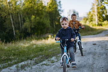 Fototapeta premium cute caucasian boys brothers are cycling together in countryside in summer time. Little one is riding runbike, elder one riding a bicycle. Image with selective focus