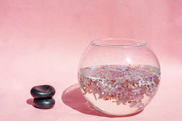 Lilac flowers float in the water. Purple and pink flowers in a glass vase stones lie next to the vase. On a pink background