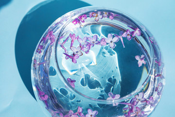 Lilac flowers float in the water. Purple and pink flowers in a glass vase. On a blue background