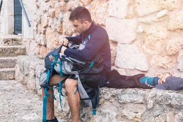 young pilgrim of the Way of Saint James sitting on the stone organizing the backpack