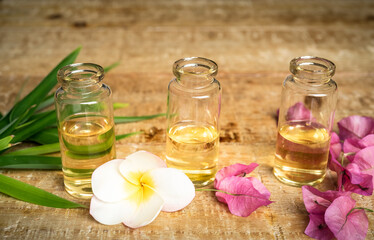 Obraz na płótnie Canvas Essential oil in small glass bottles with bamboo leaves, bougainvillea and frangipani flowers on wooden background. Selective focus. top view and copy space for text. Natural cosmetics. 